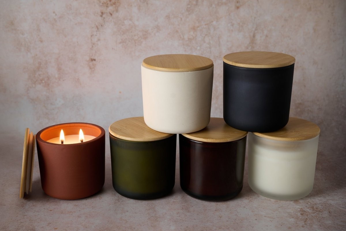 Candle vessels in a stacked grouping on a sandstone back drop. One candle on the far left is lit.