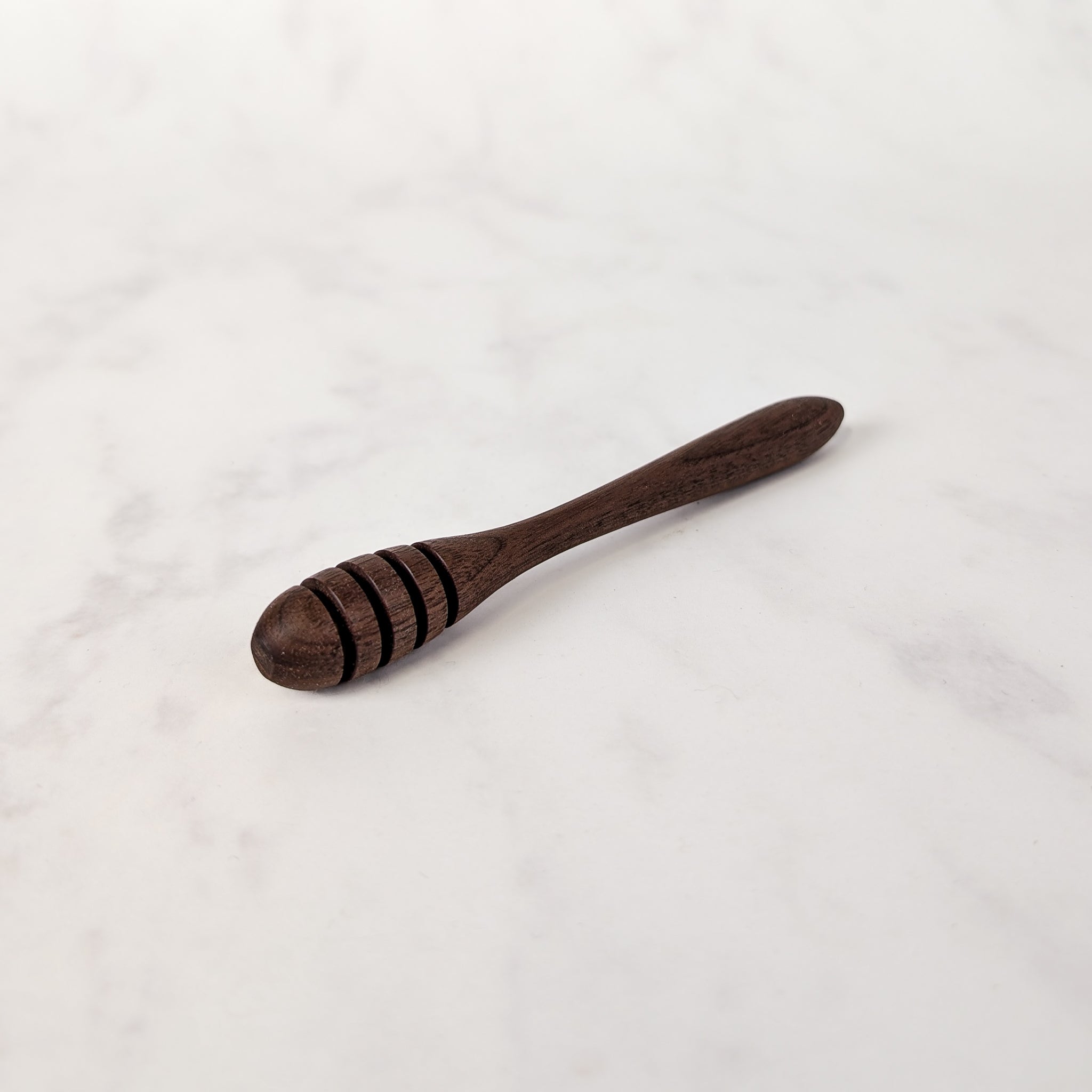 Dark wooden honey spoon on a white marble surface