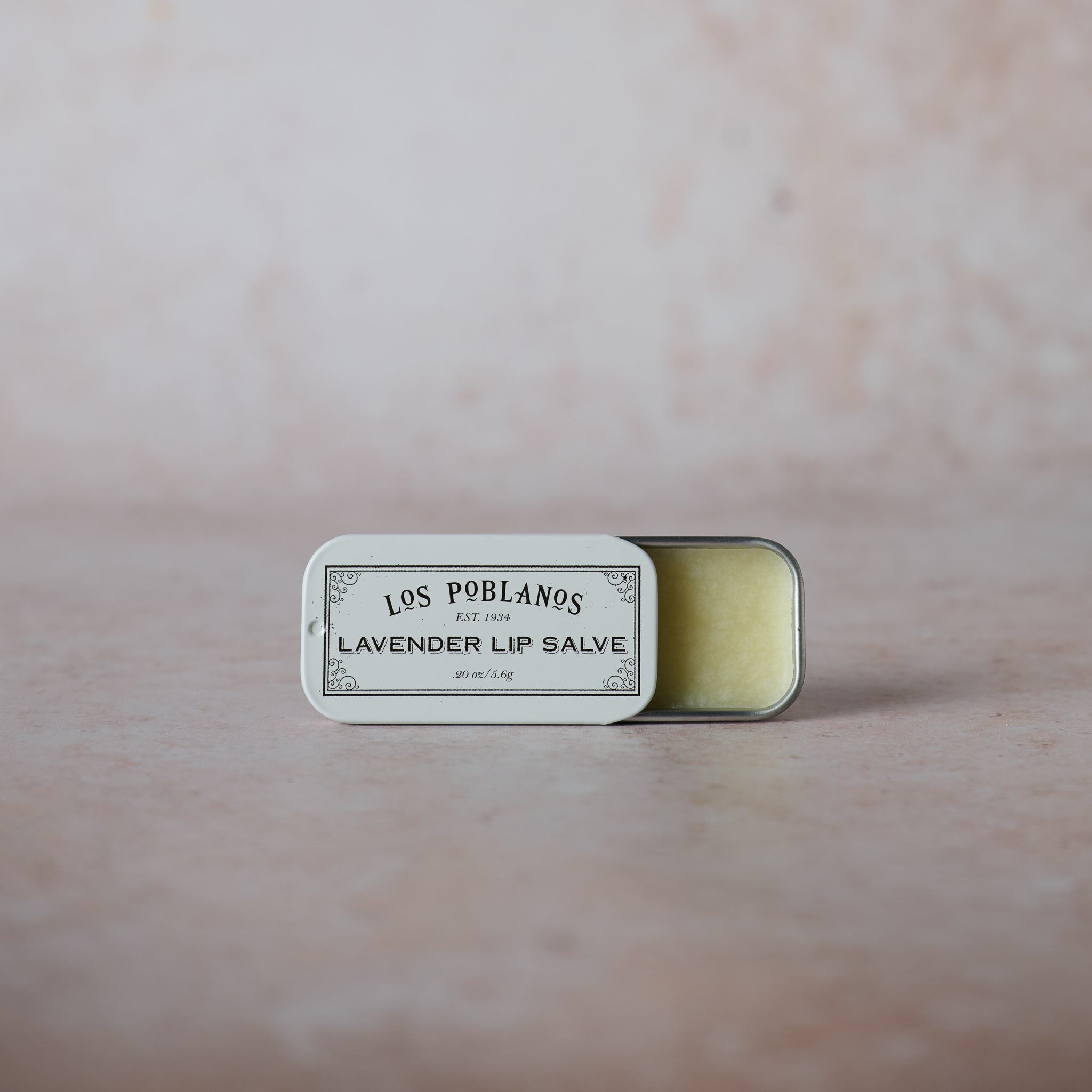 A small open tin of Los Poblanos Lavender Lip Salve on a neutral background.