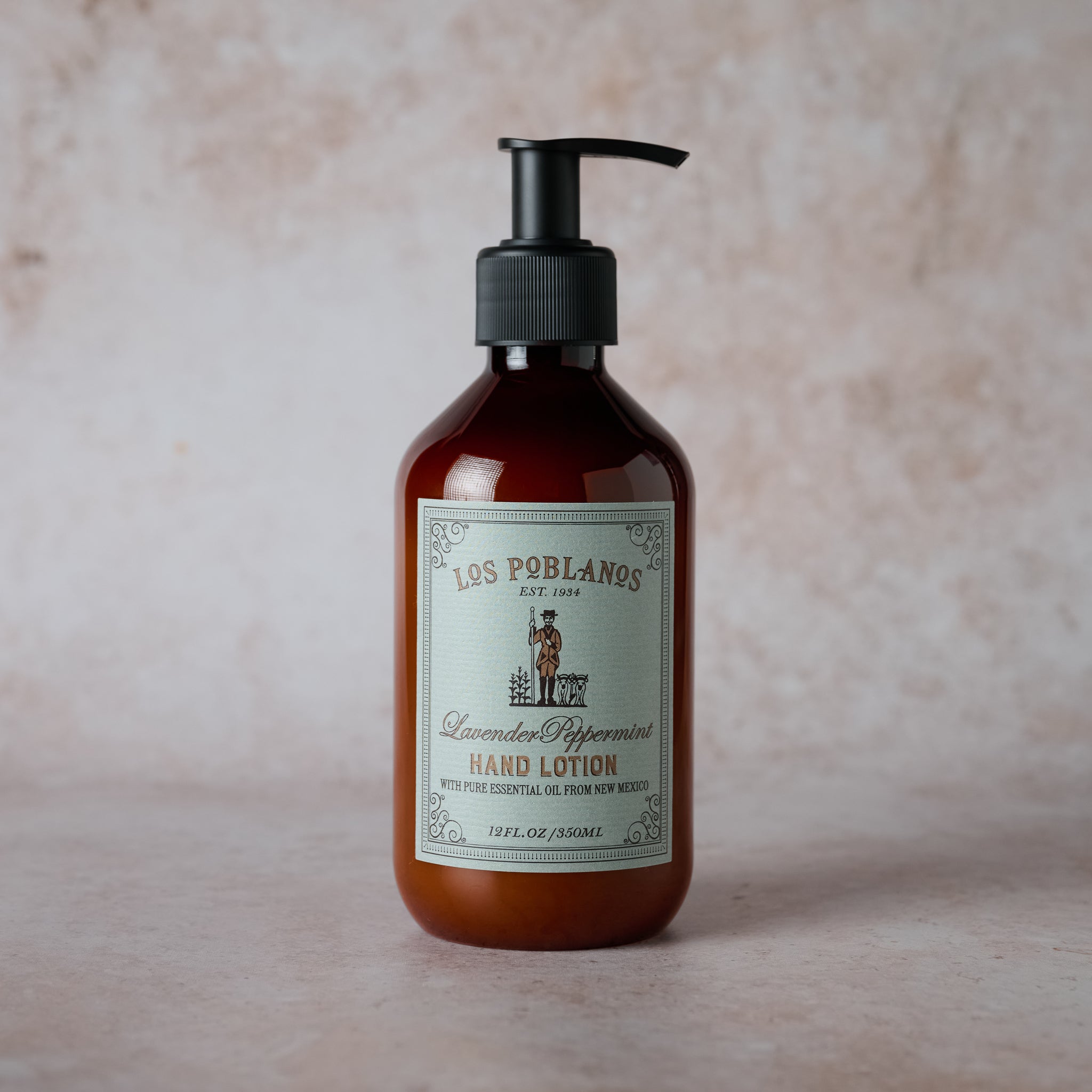 A pump bottle of Lavender Peppermint Hand Lotion by Los Poblanos, with a label featuring the brand name and the product name, placed against a textured beige background.