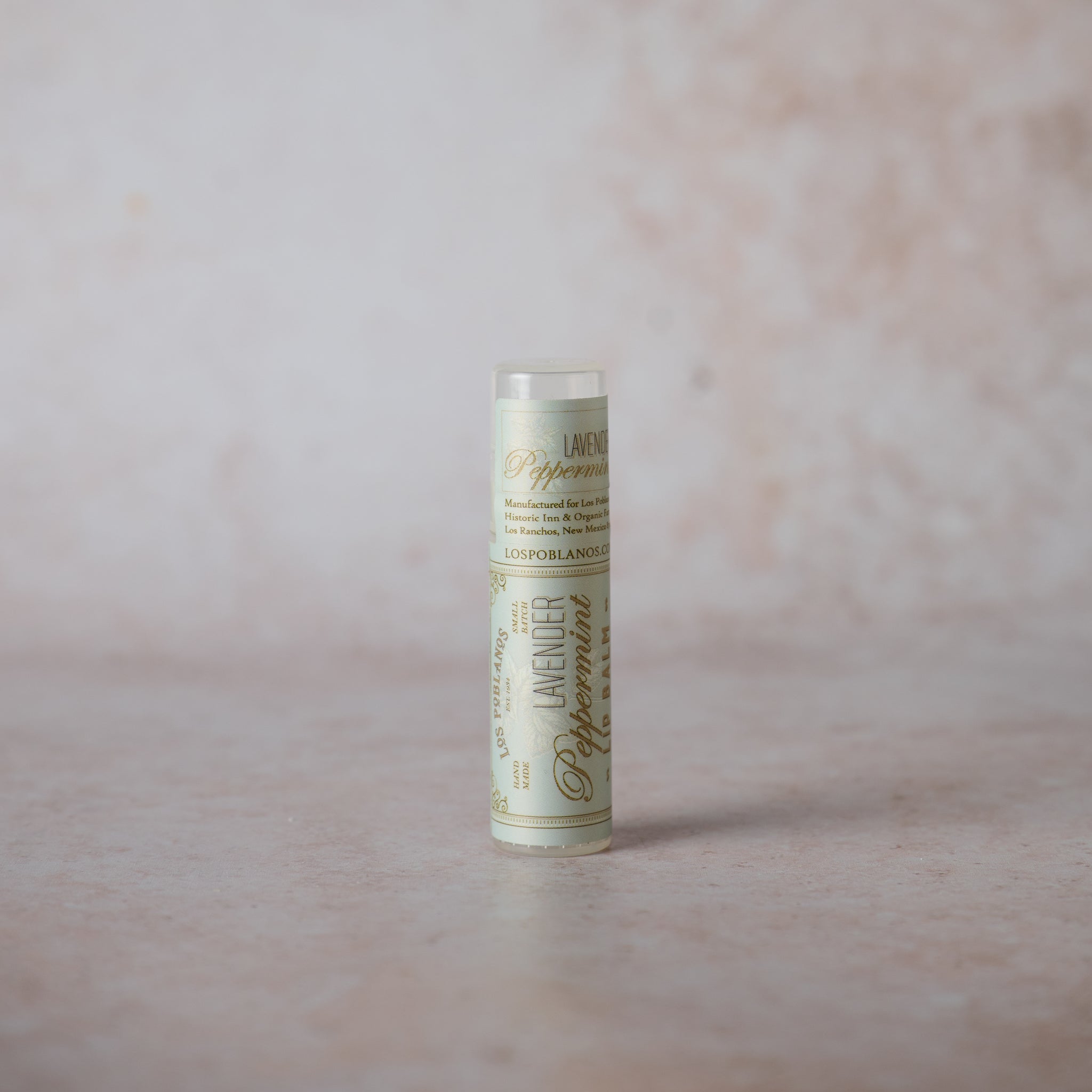 A tube of Lavender Peppermint Lip Balm against a pink background.