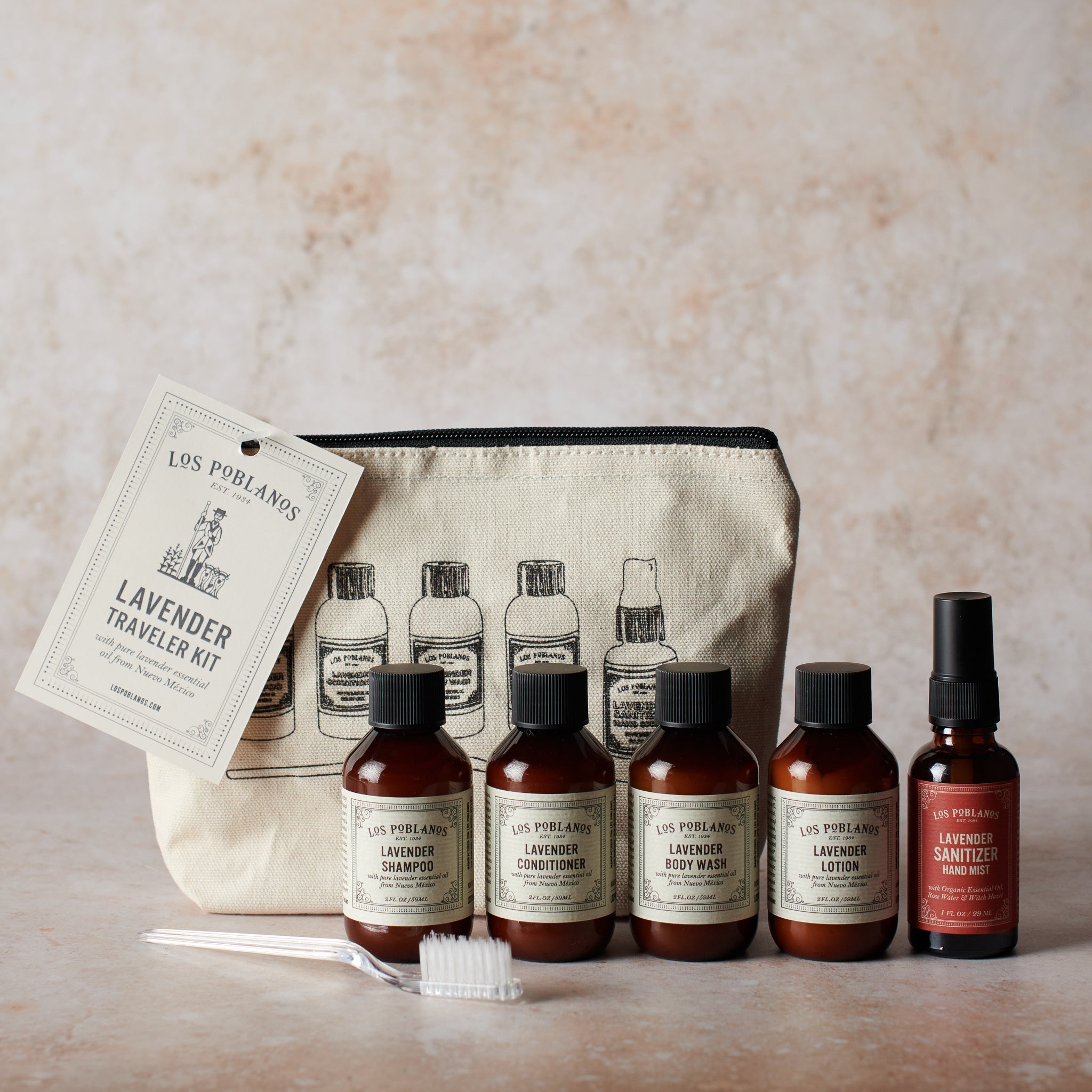 Traveler kit with five bottles of Los Poblanos signature lavender products, including shampoo, conditioner, body wash, lotion, and hand sanitizer spray, packaged in a beige cotton canvas pouch with printed text and illustrations.