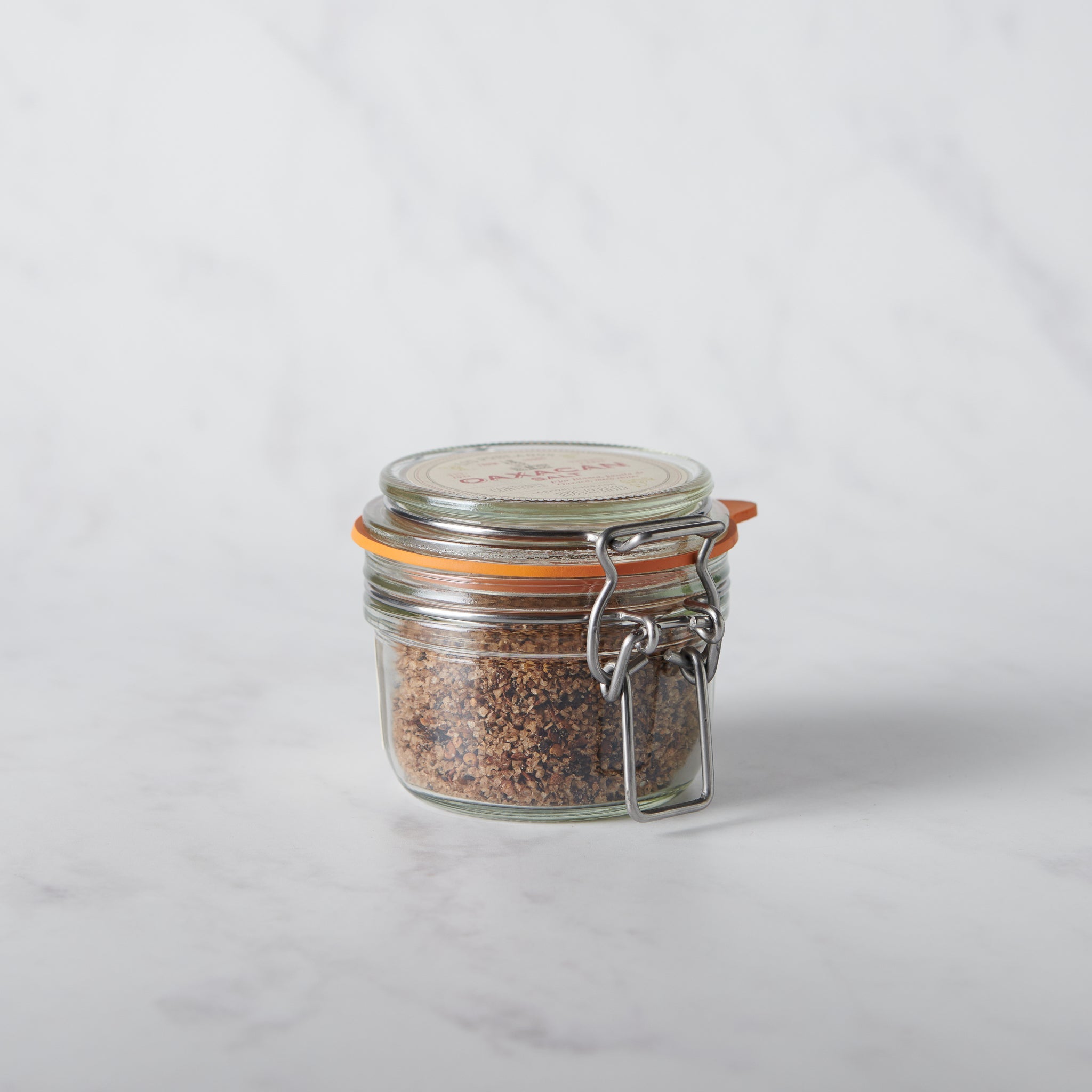 Glass jar with a metal clasp full of chile mixed salt on a white background