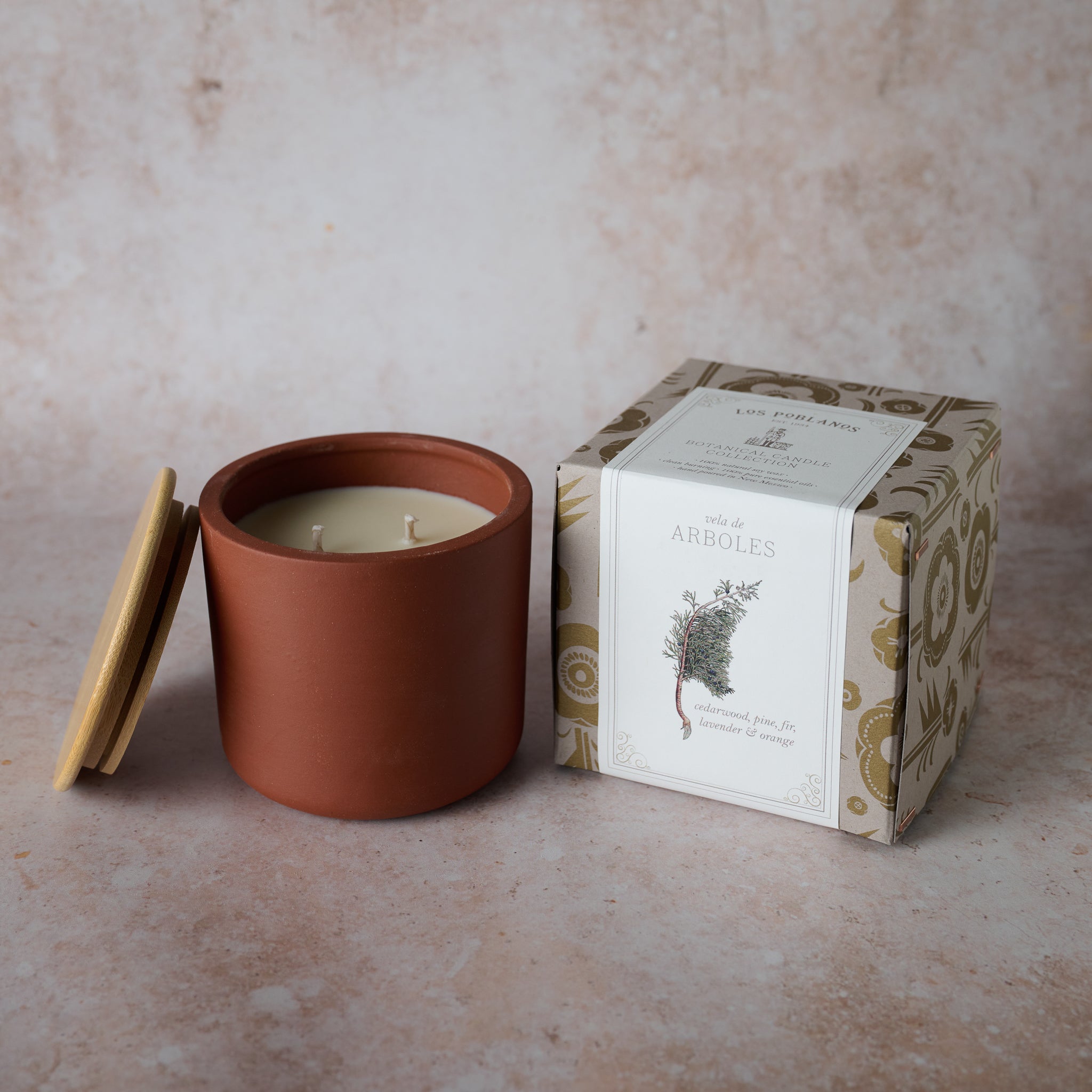 A terracotta candle vessel with a lid, next to a packaged candle, on a neutral background.