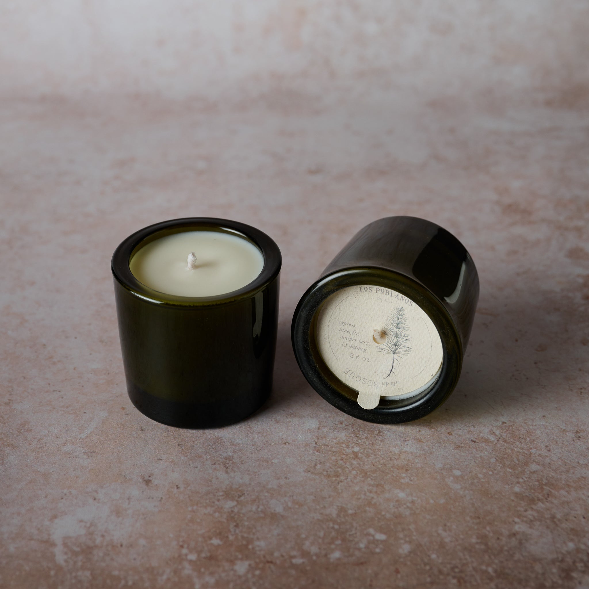 A green frosted glass candle vessel. The candle is unlit and appears to have a woodsy scent, possibly pine and fir.