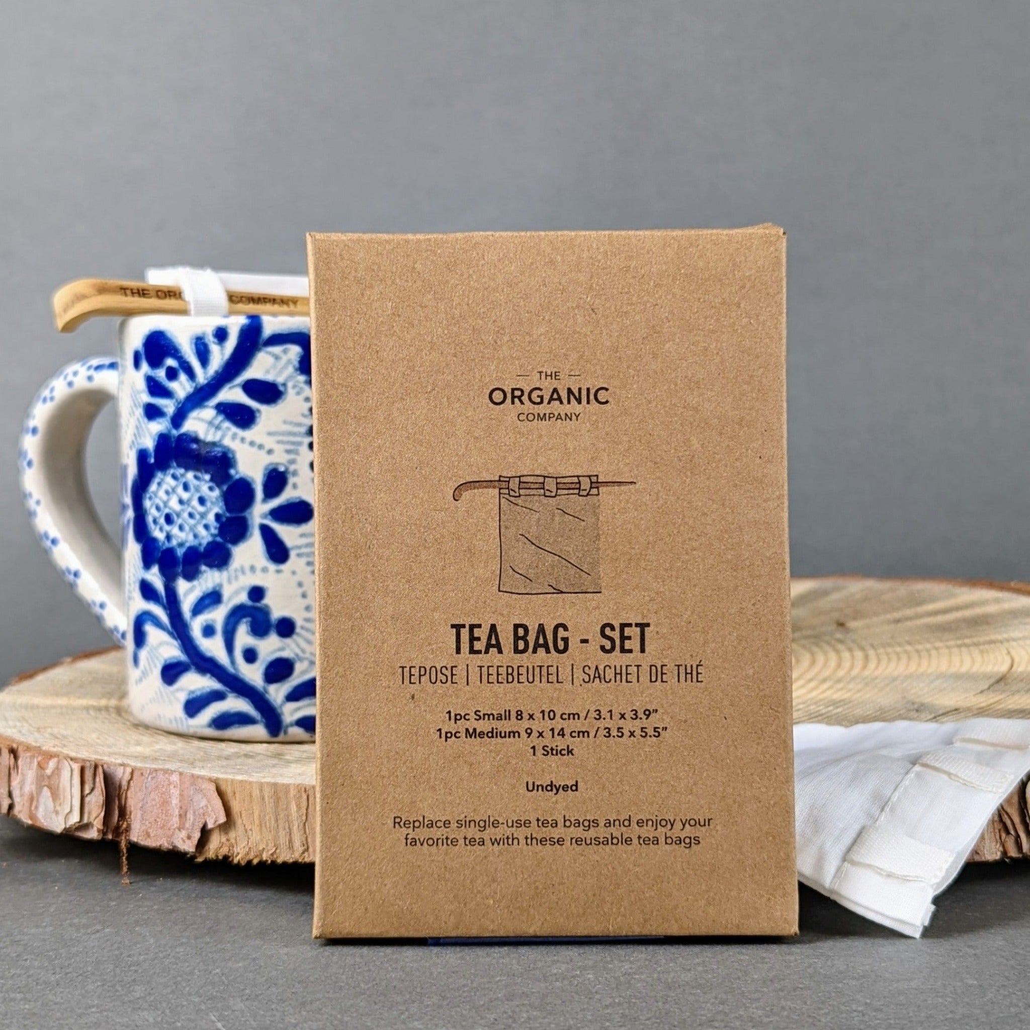 Minimalist sustainable tea accessory set: unbleached cotton tea bags and a slender wooden stick, laid out flat on a white surface