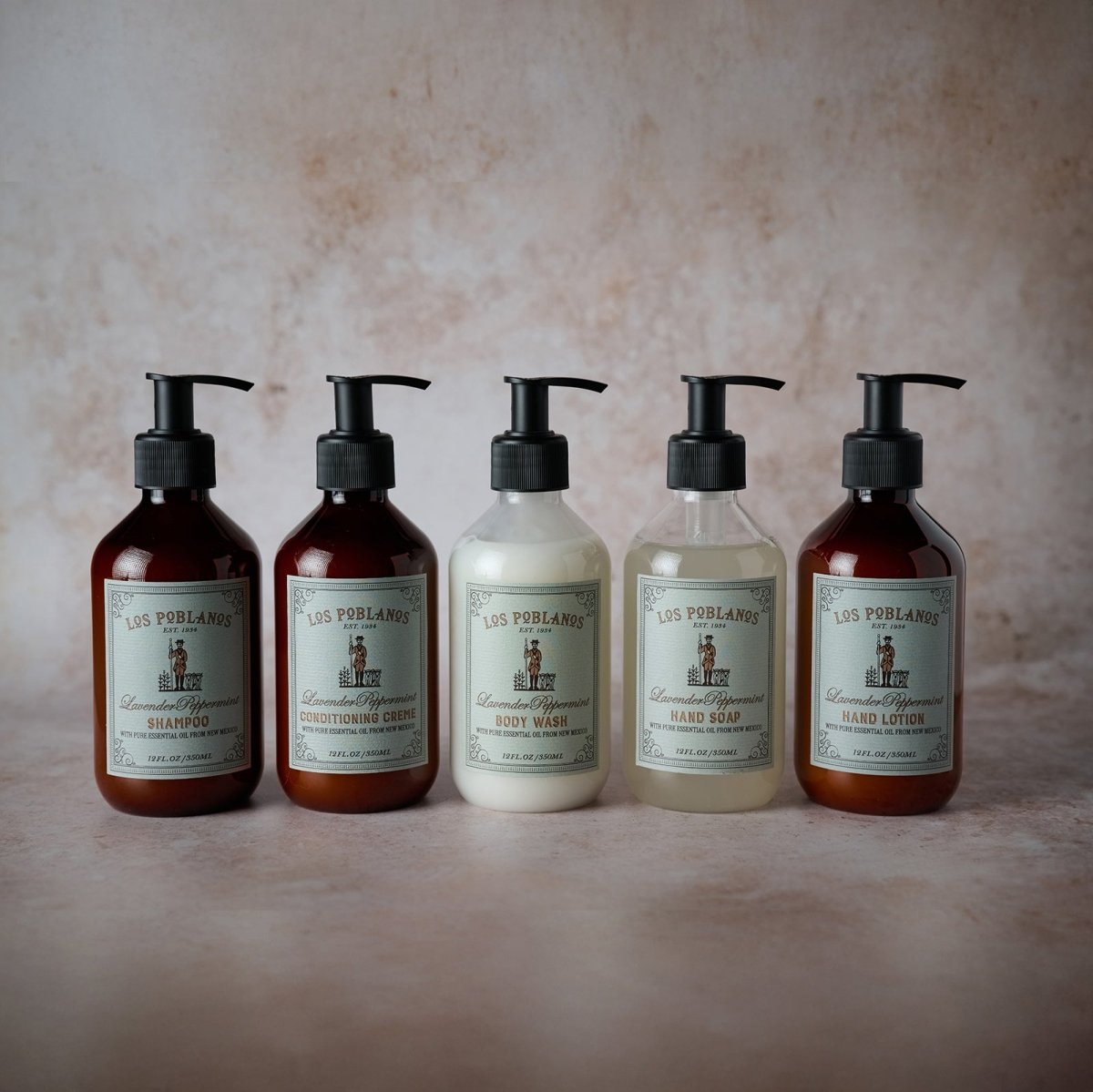 Spa-style display of Los Poblanos Lavender Peppermint body care: body wash, hand soap, scrub and more in minimalist white packaging with botanical drawings.