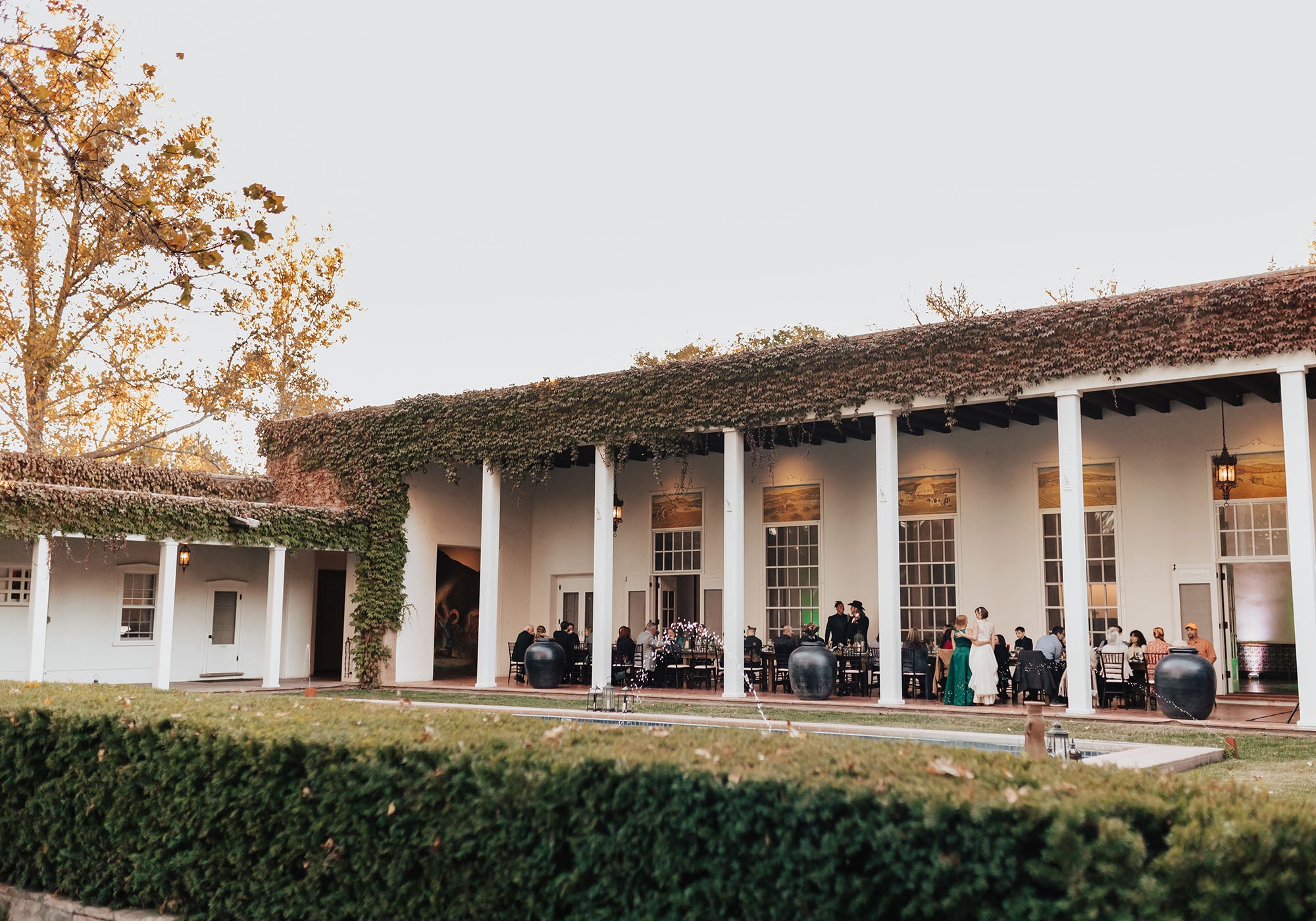 Outdoor event at a historic building with people gathered under a covered patio.