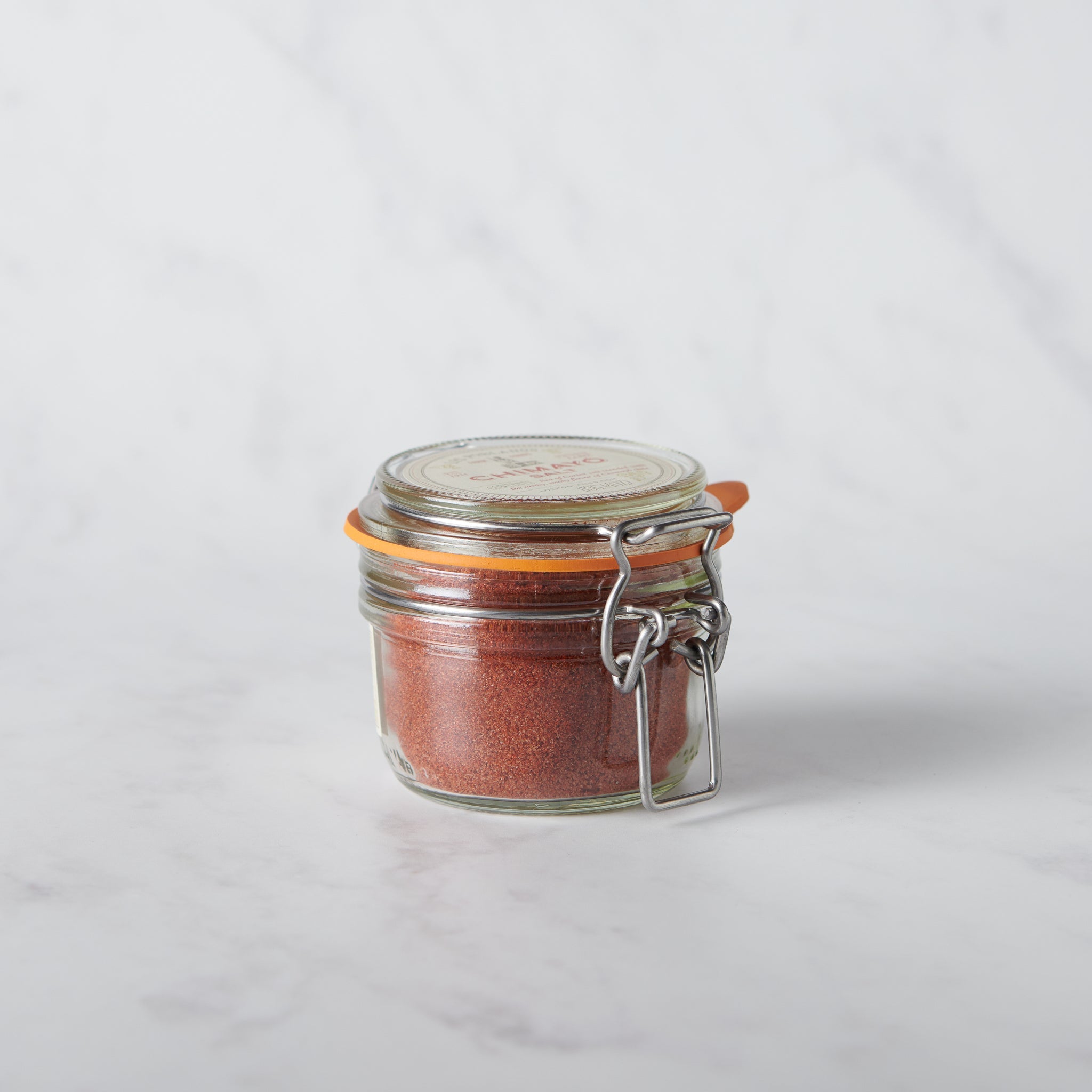 Glass jar with metal clasp full of salt blended with chile on a white background