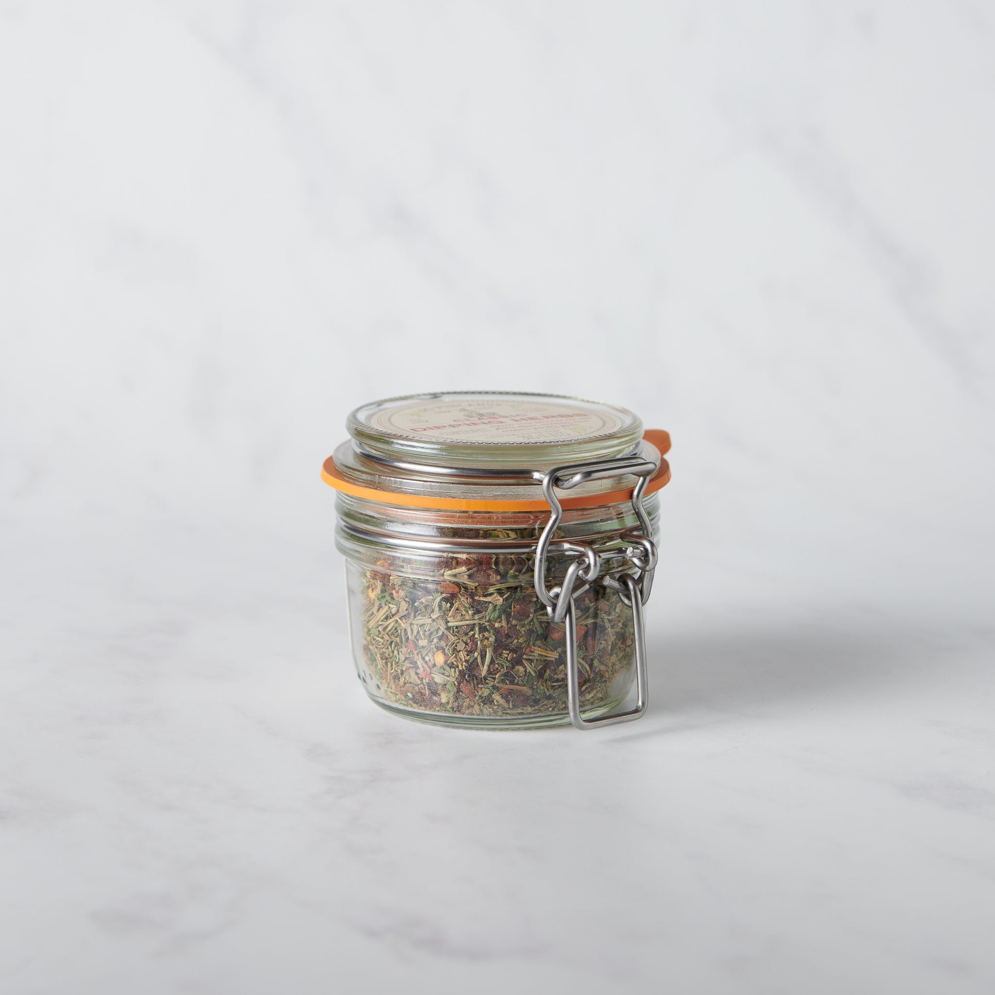 Glass jar with a metal clasp full of herbs on a white background