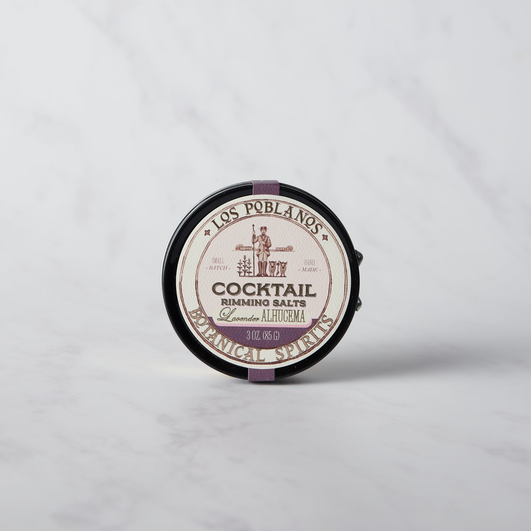 A round tin of Los Poblanos Cocktail Rimming Salt with lavender color visible through the transparent section on the lid.