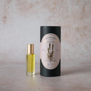 A glass vial with yellow liquid inside, next to a black cylindrical container with a label that reads 'Desert Lavender'. The background is beige.