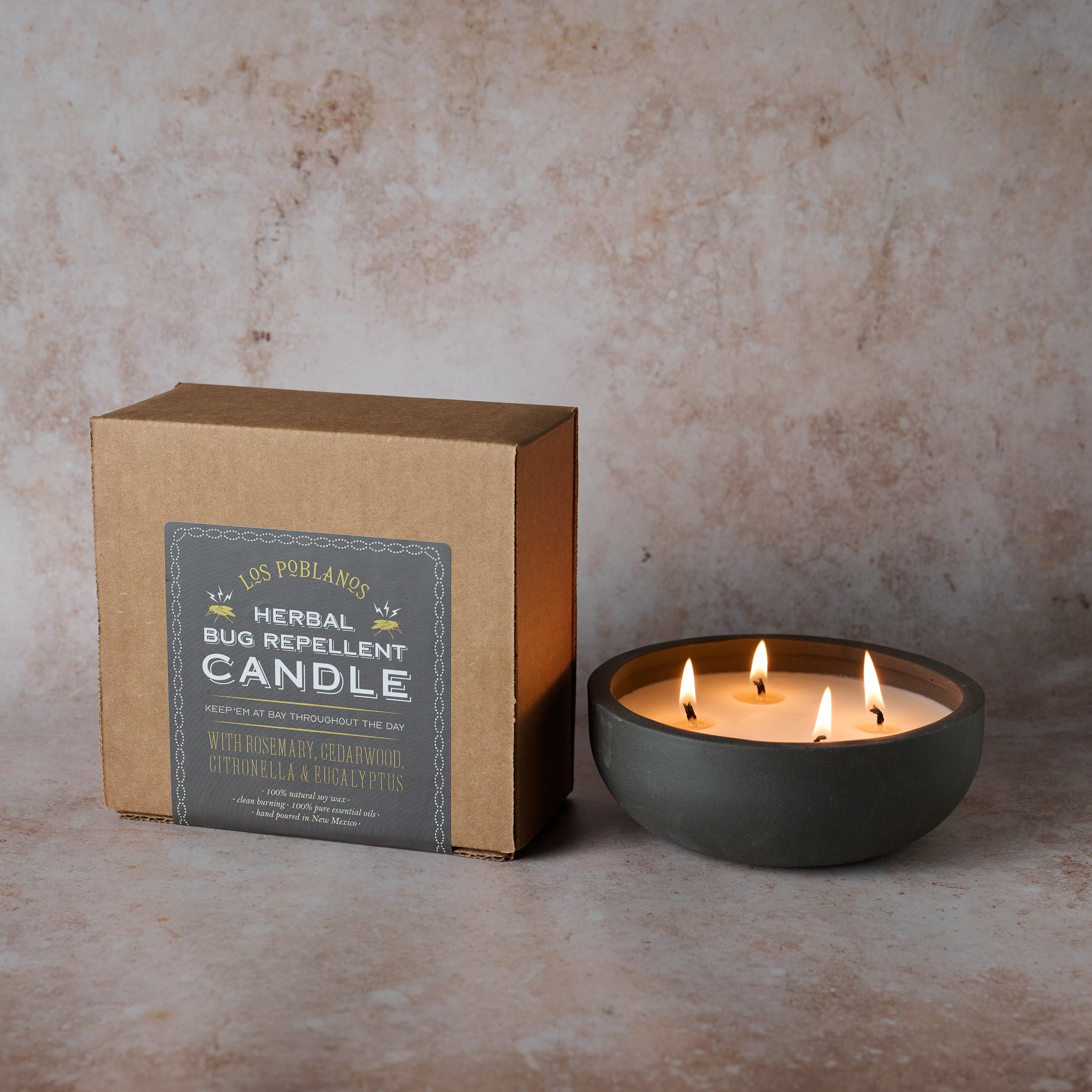A lit Herbal Bug Repellent Candle with three wicks in a black ceramic vessel, alongside its packaging box.