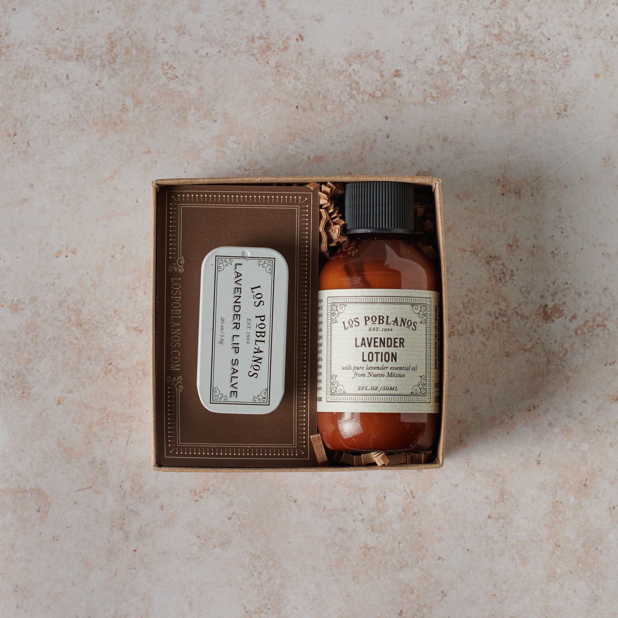 A travel-ready package containing Los Poblanos lavender lotion and lip salve, with brown labeling and a clear bottle of lotion alongside a travel tin of lip salve.