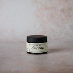 A 1.4 oz amber glass jar of Lavender Salve with a black lid, labeled with the product name and 'Lavender' text on a beige background.