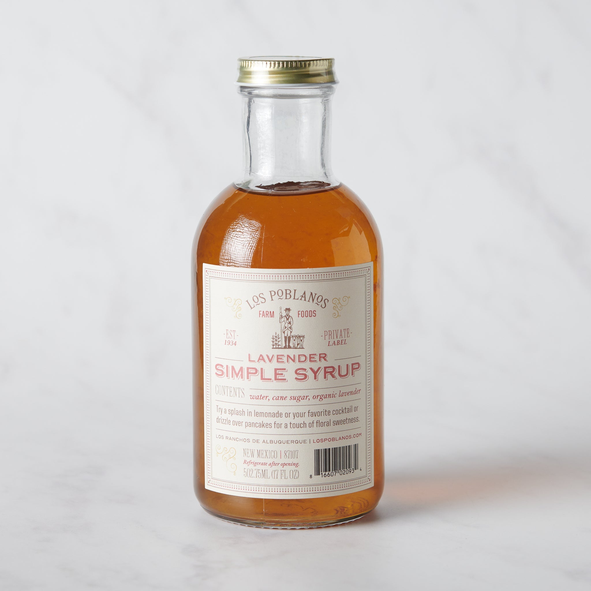 A glass bottle containing Lavender Simple Syrup on a marble surface.