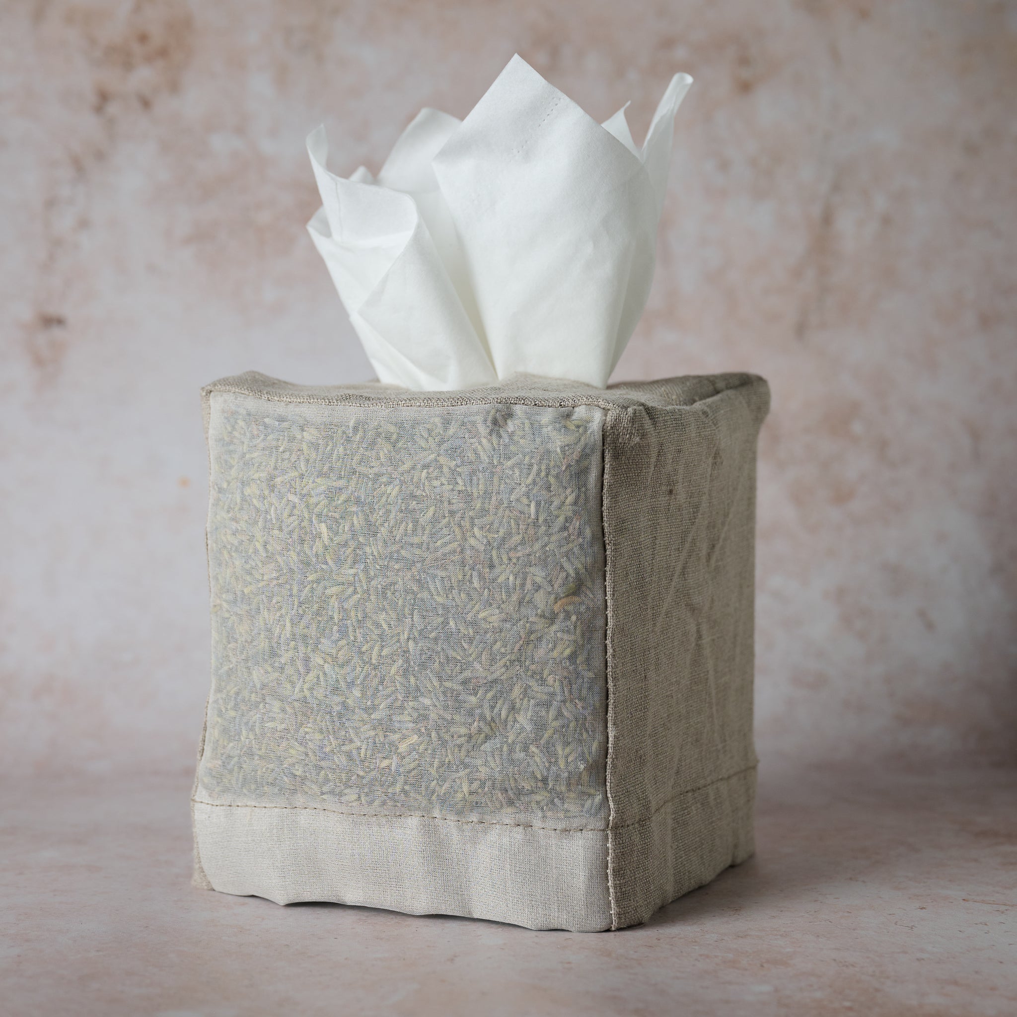 A light grey fabric tissue cover with a textured design, filled with tissues, on a textured background.