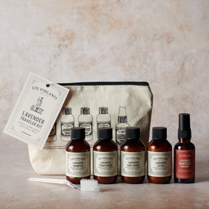 Traveler kit with five bottles of Los Poblanos signature lavender products, including shampoo, conditioner, body wash, lotion, and hand sanitizer spray, packaged in a beige cotton canvas pouch with printed text and illustrations.