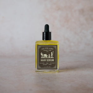 A glass bottle with a black dropper containing yellow liquid, labeled as 'HAIR SERUM' with an illustration of a farmer and crops.