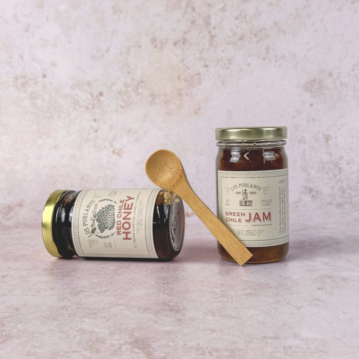 Two jars of honey and jam with wooden spoons on a light pink background