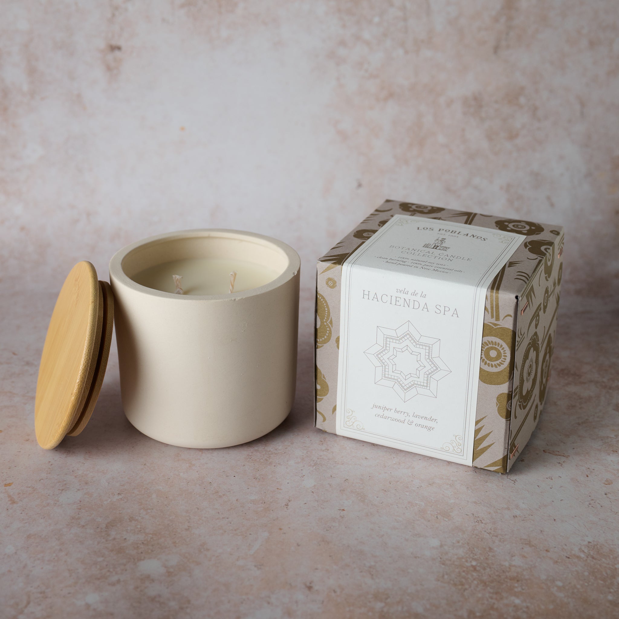 A soy wax candle with cedarwood and orange scent, presented in a white porcelain jar with a wooden lid, next to its packaging box which has 'Hacienda Spa' branding.