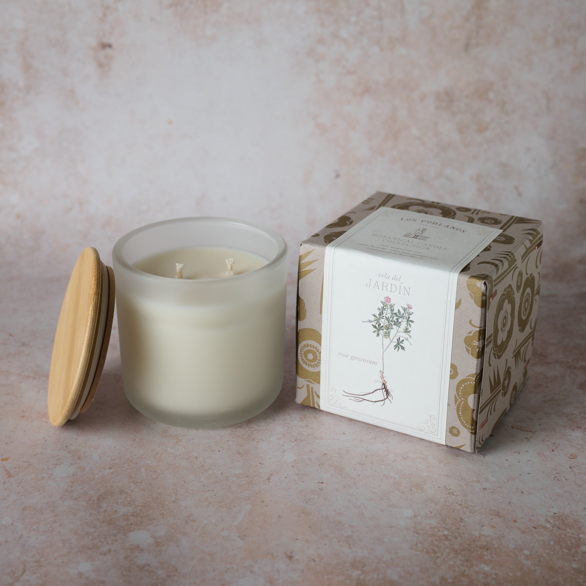 A frosted white glass candle jar with a wooden lid next to a box that has a botanical illustration. The candle is unscented and appears to be natural soy wax.